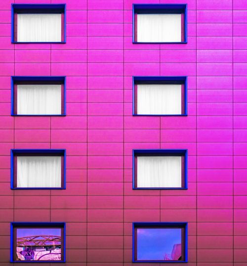 Pink building facade with symmetrical windows and reflections, a striking urban architectural design.