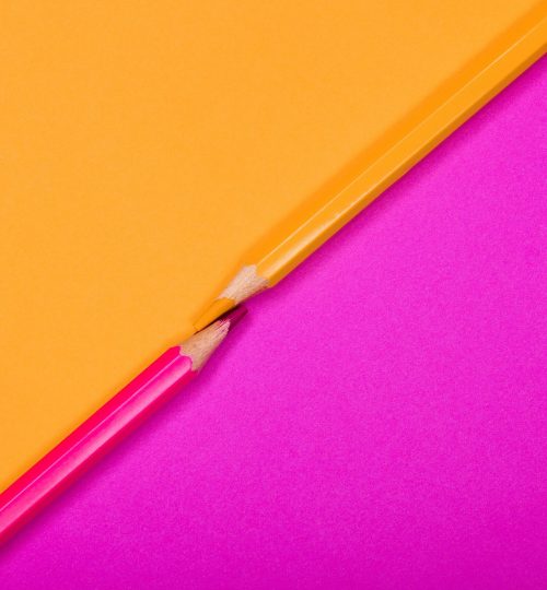 Two colored pencils on bright pink and yellow backgrounds, creatively arranged.